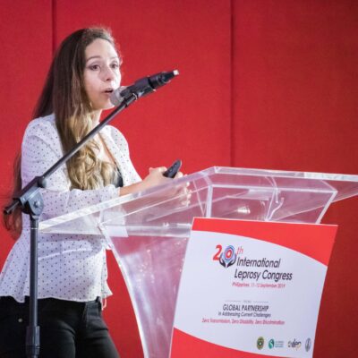 Alice Cruz stands behind a podium and speaks at the International Leprosy Congress. Photo credit: Andie Tucker